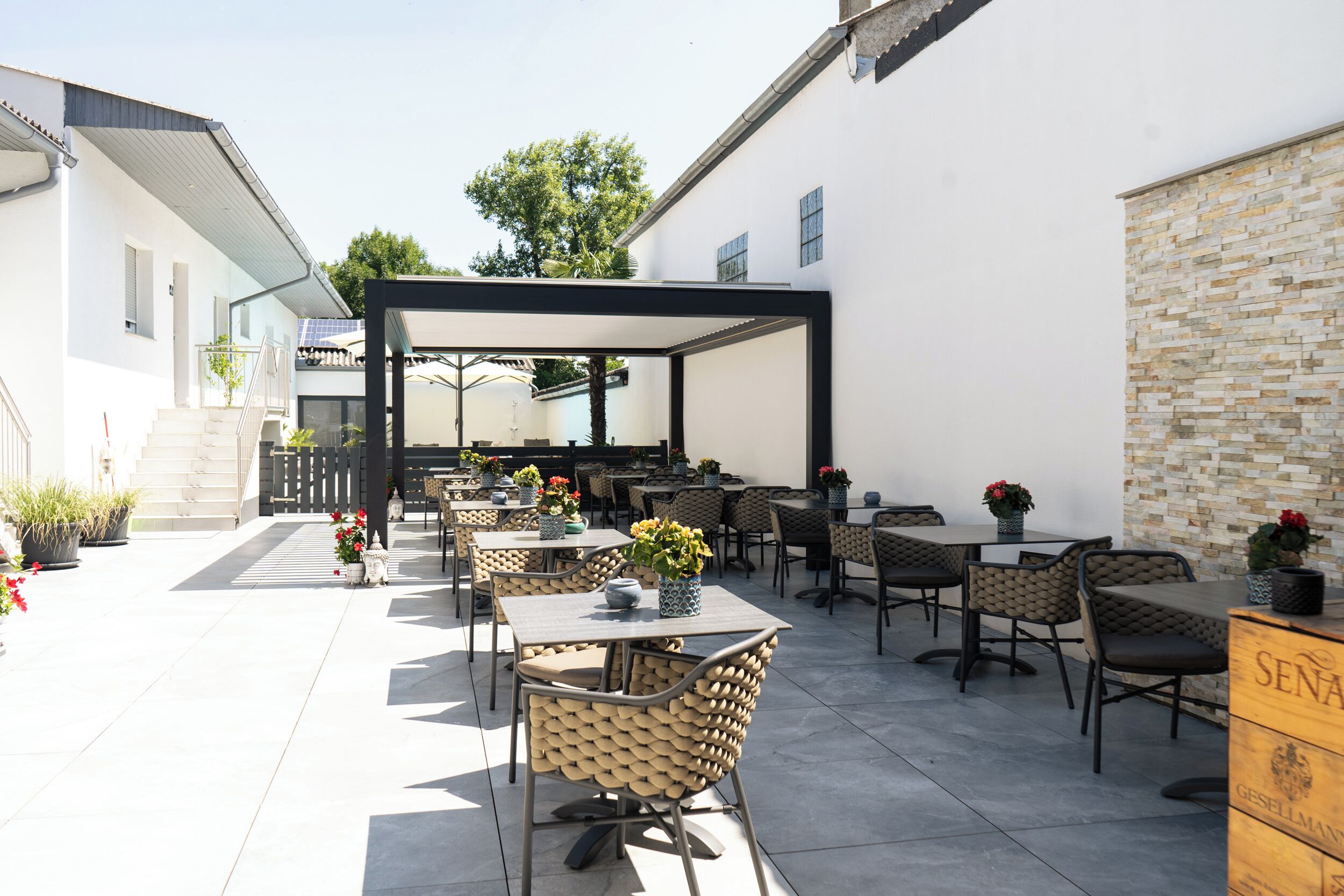 An outdoor patio with multiple tables and chairs, a covered seating area, and a stone wall.