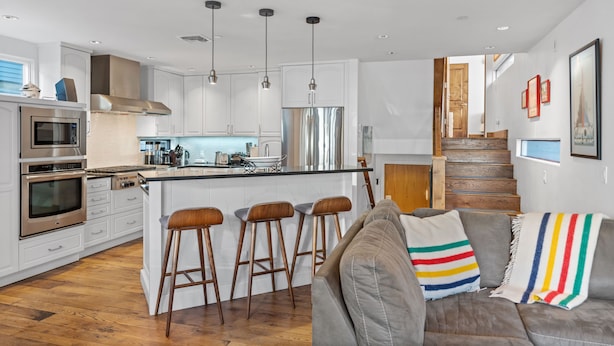 Una cocina moderna con armarios blancos, electrodomésticos de acero inoxidable y una isla central con taburetes.