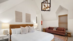 A bedroom with a large bed, a wooden headboard, two bedside tables with lamps, a red sofa, and a patterned rug.
