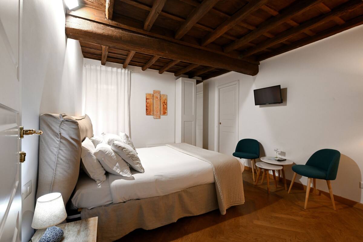 Een slaapkamer met een bed, twee stoelen, een kleine tafel, een televisie en kunst aan de muur.