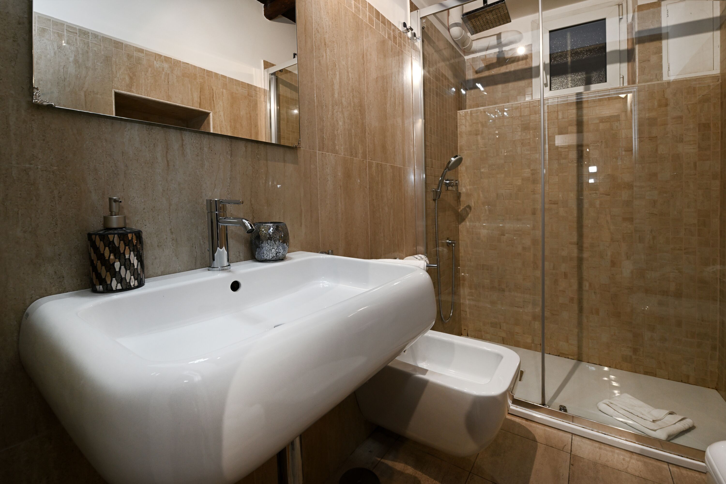 A bathroom with a large white sink, a glass-enclosed shower, and a small white bathtub.