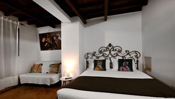 Een slaapkamer met een groot bed, een kleinere bank, een nachtkastje en een schilderij aan de muur.