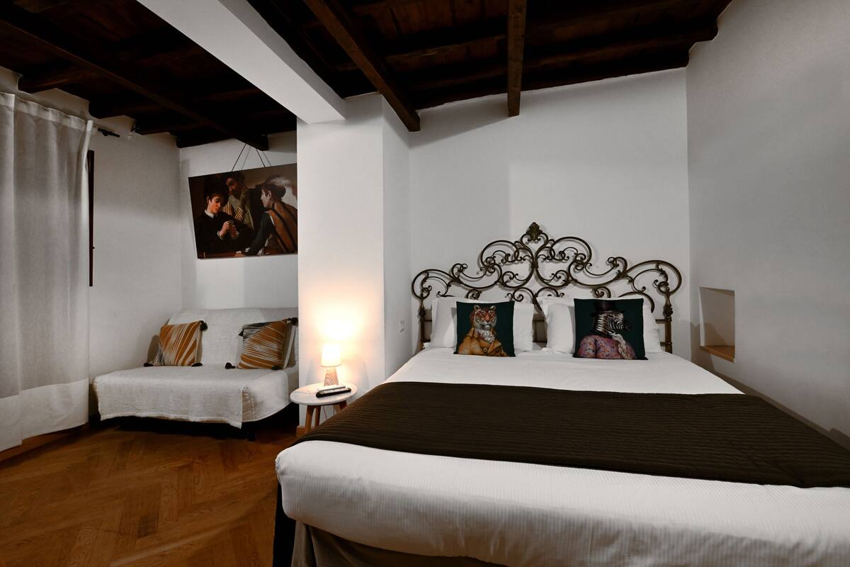 Een slaapkamer met een groot bed, een kleinere bank, een nachtkastje en een schilderij aan de muur.