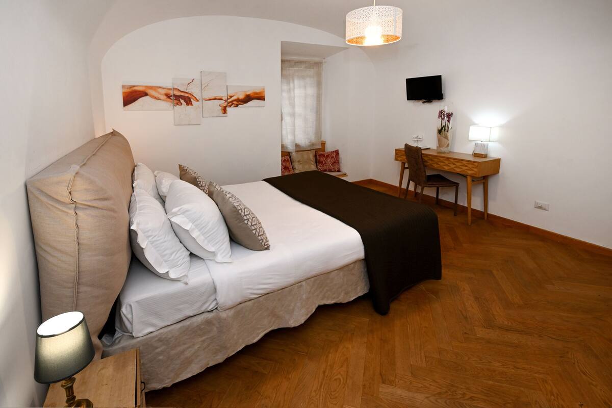 Een slaapkamer met een bed, een bureau, een stoel, een lamp en kunst aan de muur.