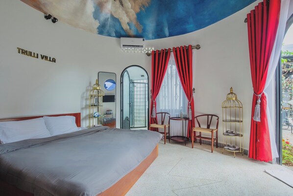 Un dormitorio con cama, escritorio, sillas, cortina roja, jaula de pájaros y un mural en el techo.