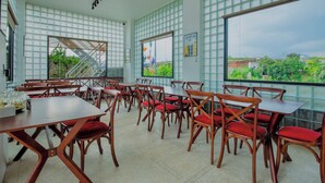 A dining area with wooden tables and chairs, large windows with a view of greenery, and a staircase leading to an upper level. - Trulli Villa Homestay (Don Duong)