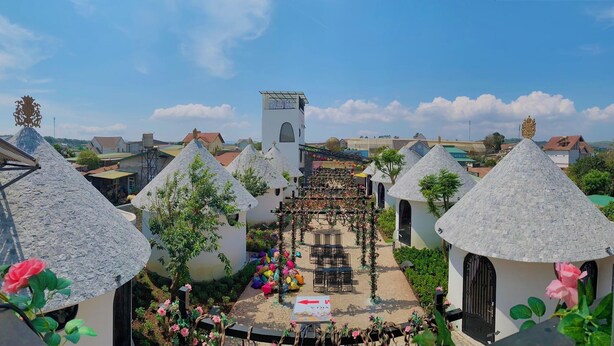 A courtyard with thatched-roof buildings, a central tower, and a sign indicating a restaurant. - Trulli Villa Homestay (Don Duong)