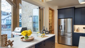 A modern kitchen with a large island, a stainless steel refrigerator, and a stone wall. - New + Contemporary + Neighborhood Gondola | Dala Horse Lodge (Steamboat Springs)