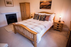 A bedroom with a wooden bed, a fireplace, a nightstand with a lamp, and a painting on the wall. - Abbey Farm House (Brampton)