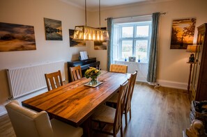 A dining area with a wooden table, chairs, a piano, and artwork on the walls. - Abbey Farm House (Brampton)