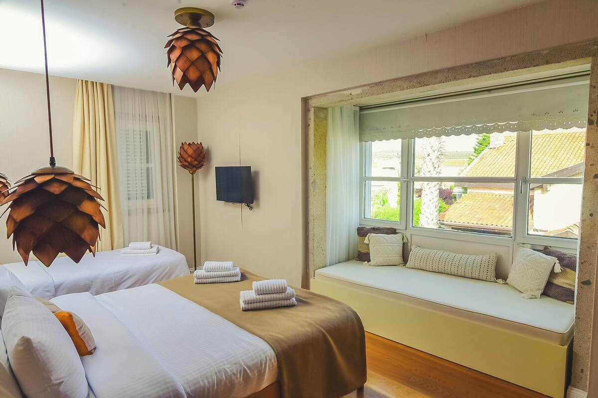A hotel room with two beds, a large window with a view, and a unique ceiling light fixture.