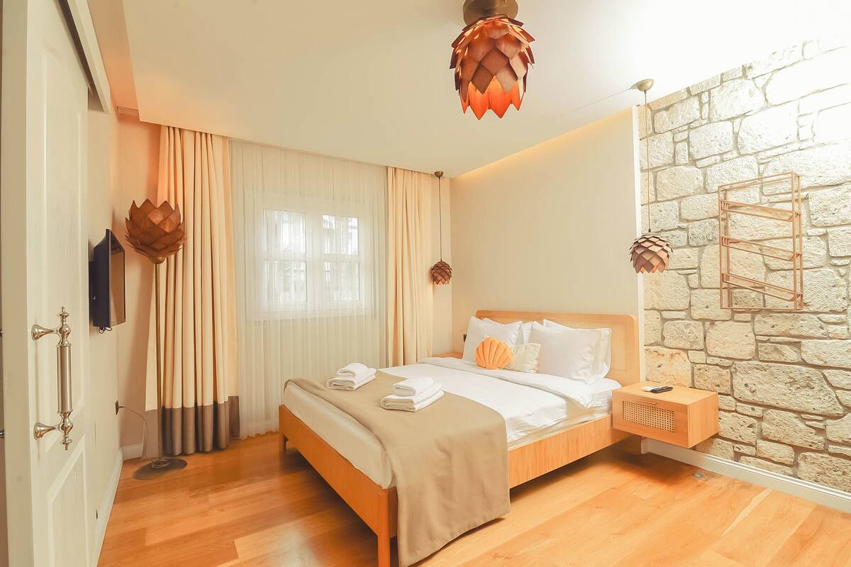 A hotel room with a wooden bed, a stone wall, and a modern pendant light.
