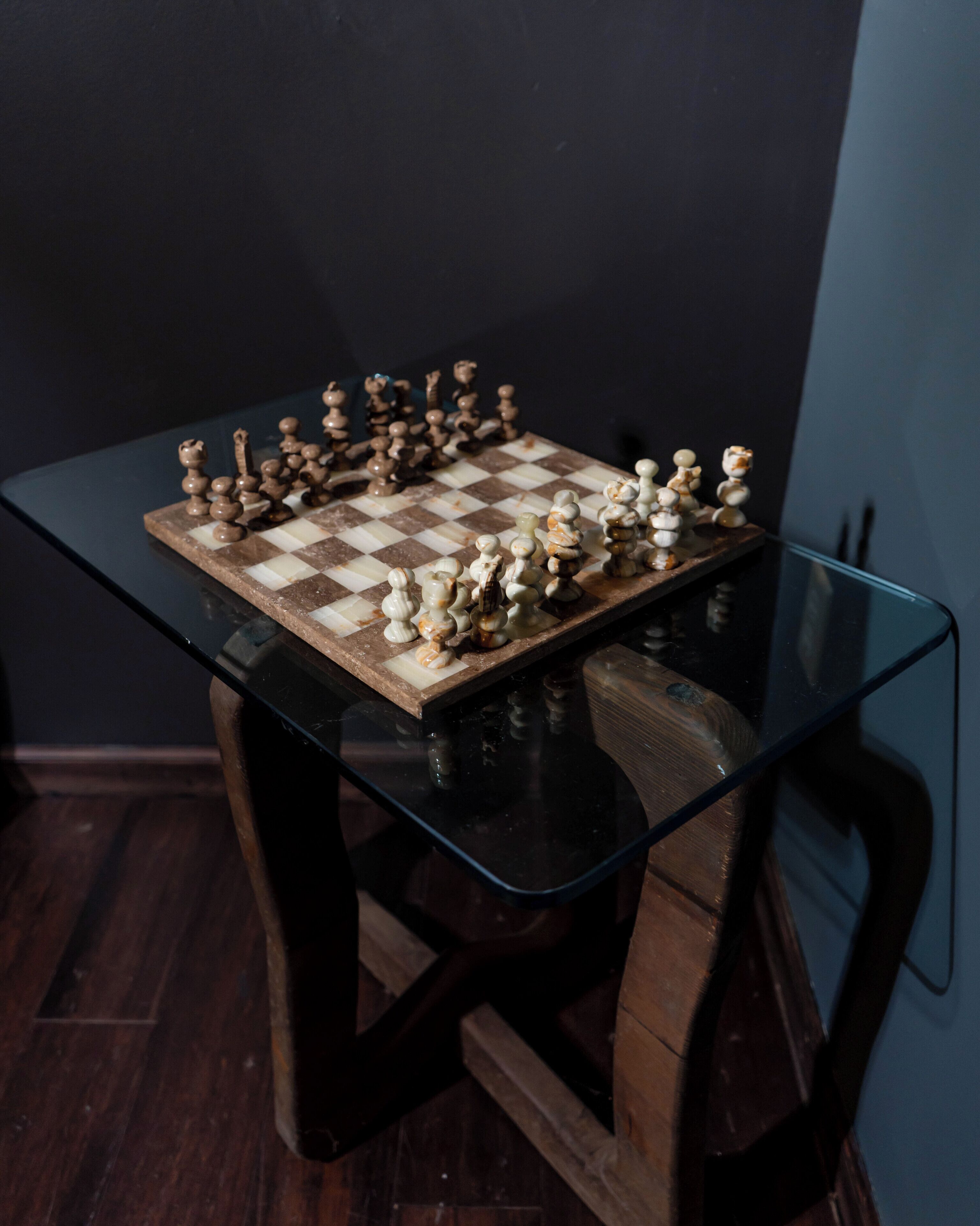 A chessboard on a glass-top table with wooden legs.