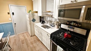 Une cuisine de taille réduite avec des meubles blancs, une cuisinière en acier inoxydable, un four à micro-ondes et un évier.