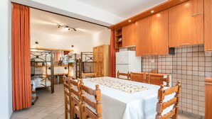 A modern kitchen with wooden cabinets, a dining table with chairs, and a refrigerator. - Three Bedroom Apartment 7-9 Adults First Floor (Paros)