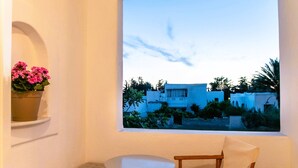 A balcony with a table and chairs, a potted plant, and a view of buildings and greenery. - Three Bedroom Apartment 7-9 Adults First Floor (Paros)