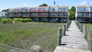 A wooden boardwalk leading to a beachfront property with multiple-story buildings, each with balconies and a clear view of the ocean.