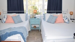 A bedroom with two beds, a nightstand, and a window with curtains.