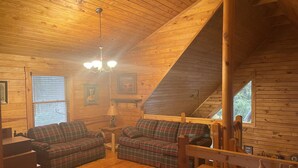L’intérieur chaleureux d’un chalet avec un plafond en bois, des canapés à carreaux, une table en bois et des tableaux encadrés accrochés aux murs.