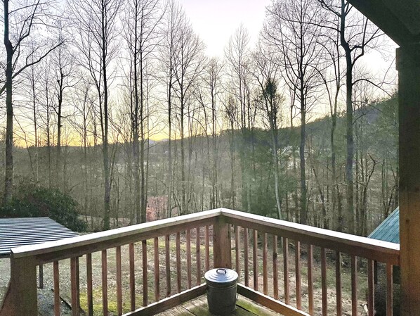 A wooden deck with a metal container, surrounded by trees and a hilly landscape.
