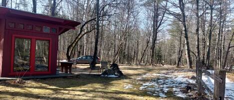 A cabin with a red exterior, a picnic table, and a car parked nearby.