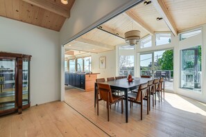 Un comedor amplio con una mesa grande y sillas, una cocina al fondo y ventanas grandes que ofrecen vistas al exterior.