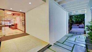 A modern hotel lobby with a glass wall, a reception area, and a pathway leading outside. - Hotel Twin Tulips HSR Layout (Bengaluru)