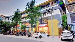 A modern building with multiple floors, a variety of shops on the ground floor, and several parked cars and motorcycles. - Hotel Twin Tulips HSR Layout (Bengaluru)