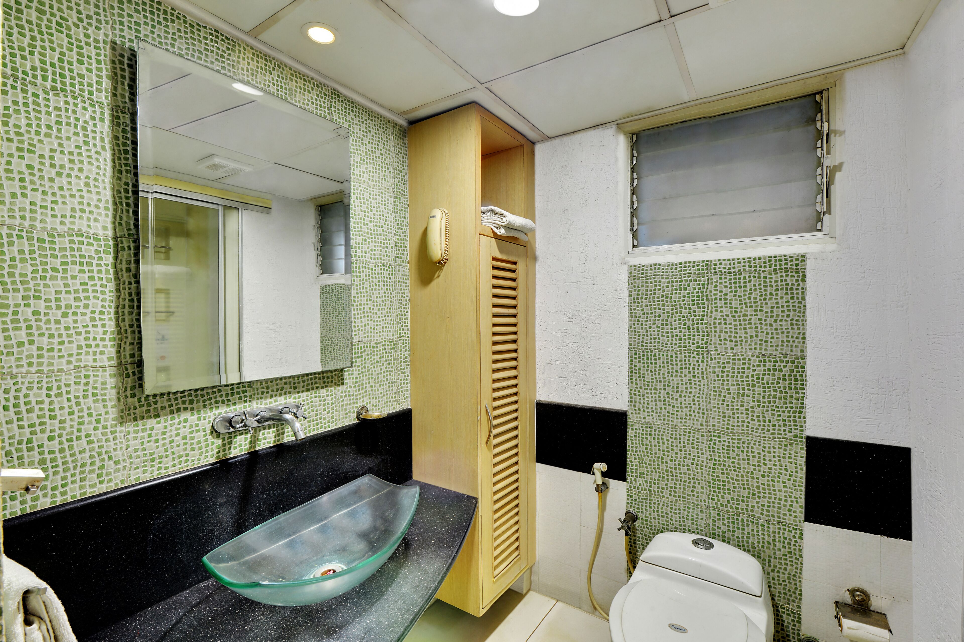A bathroom with a glass vessel sink, a wooden cabinet, a toilet, and a mirror.