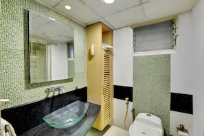 A bathroom with a glass vessel sink, a wooden cabinet, a toilet, and a mirror.