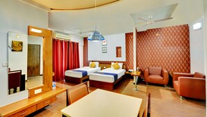 A hotel room with two beds, a sofa, a dining table, a mirror, and a ceiling fan. - Hotel Twin Tulips HSR Layout (Bengaluru)