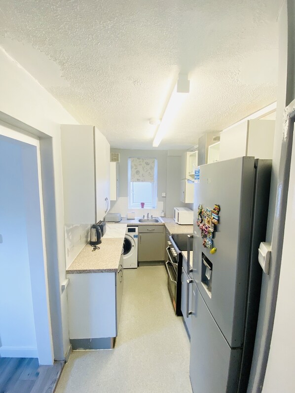 A compact kitchen with a washing machine, a refrigerator, and a microwave.