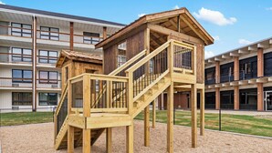 A playground with wooden play structures and a building in the background.