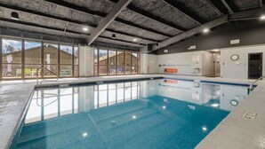 An indoor swimming pool with clear glass walls, a concrete ceiling, and visible windows to the outside.