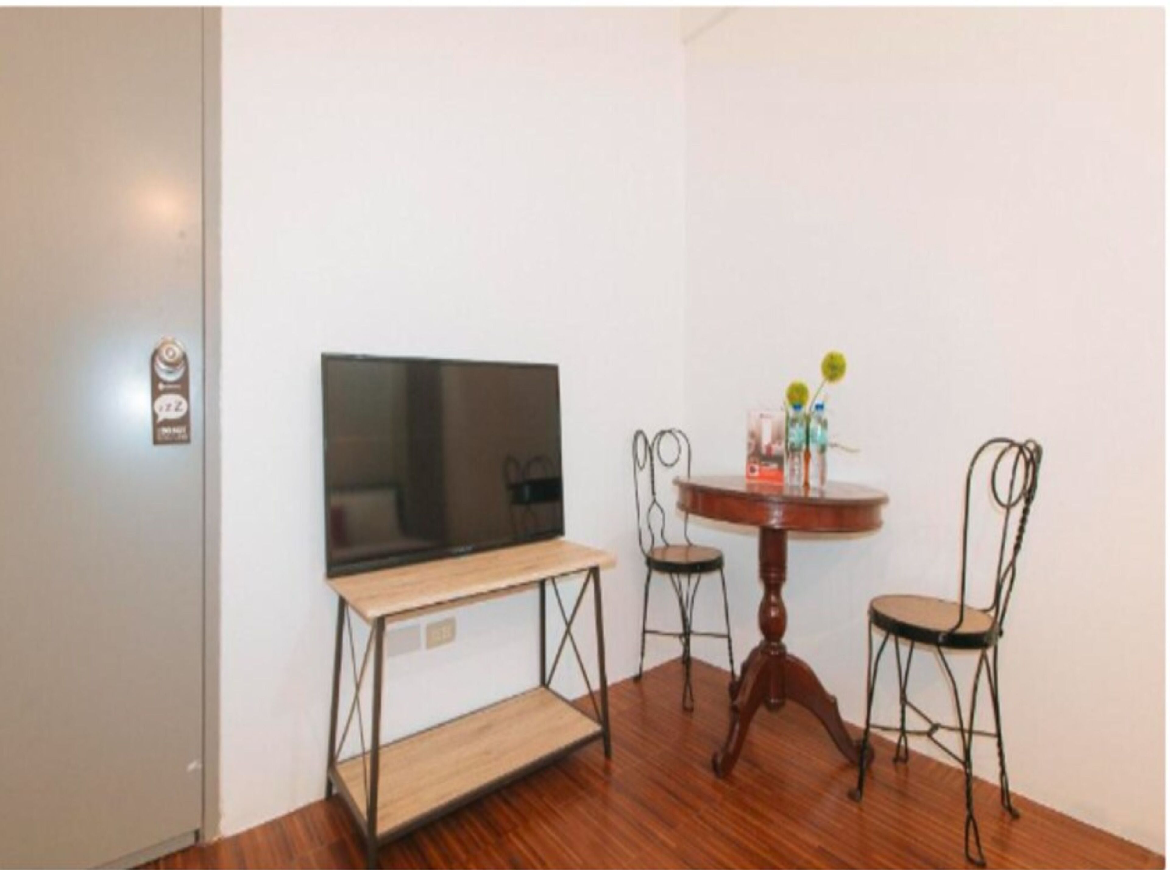 Una habitación con una televisión de pantalla plana en la pared, una mesa de madera con dos sillas y un estante pequeño.