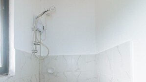 Baño con paredes de mármol blanco y ducha con cabezal de ducha manual.
