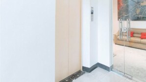 Un interior moderno con un divisor de vidrio corredera que da a un espacio de estar, un sofá beige con cojines rojos y un cuadro abstracto contemporáneo en la pared.
