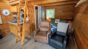 A cozy cabin interior with a wooden interior, a ladder, a bed, a chair, and a small kitchenette.