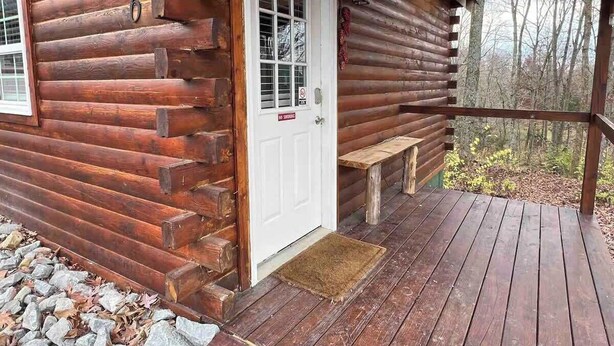 A log cabin with a wooden deck and a white door.