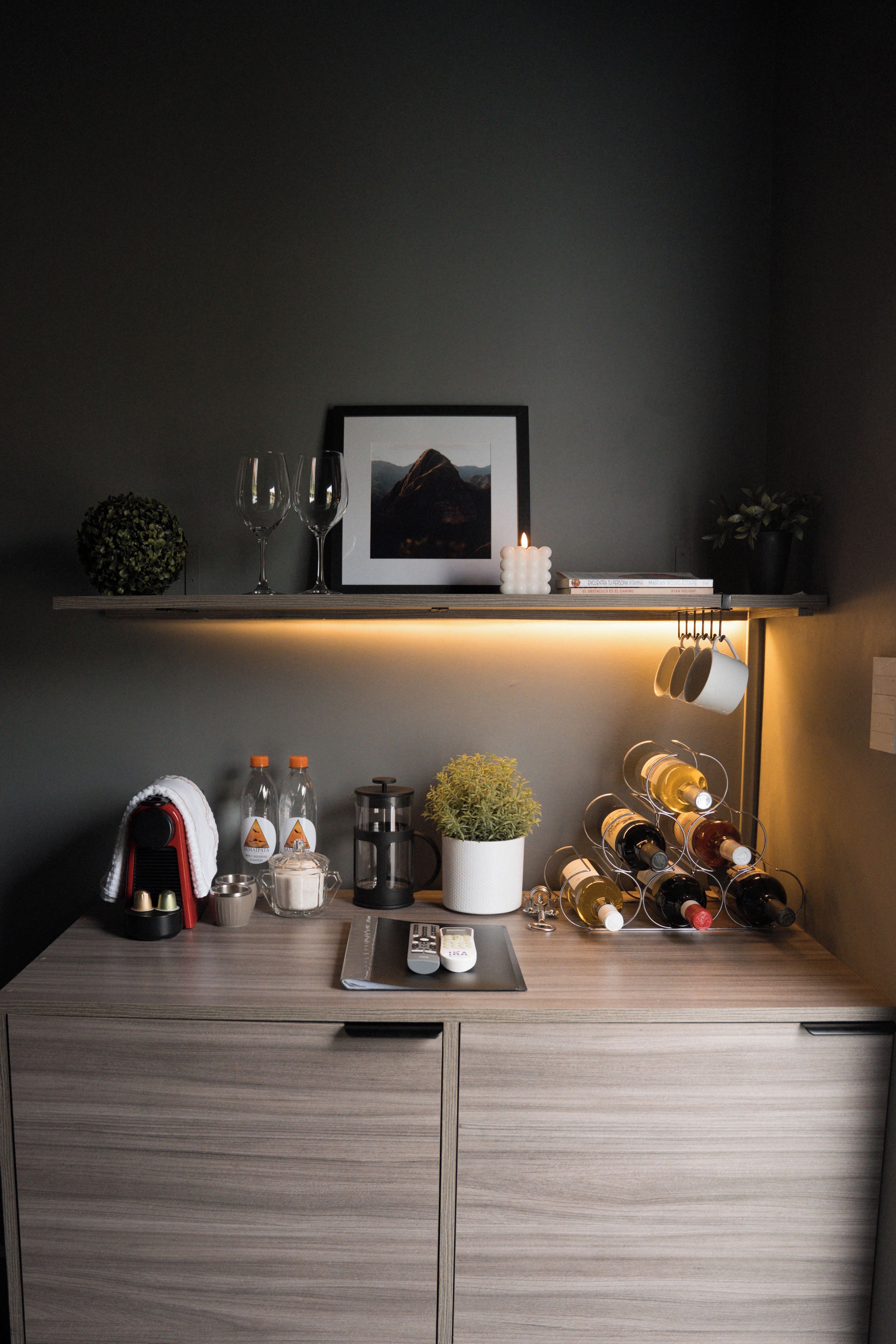 Siisti ja järjestelmällinen huone, jossa on puinen työpöytä, seinälle kiinnitetty viiniteline, kahvinkeitin ja seinällä oleva kehystetty kuva.