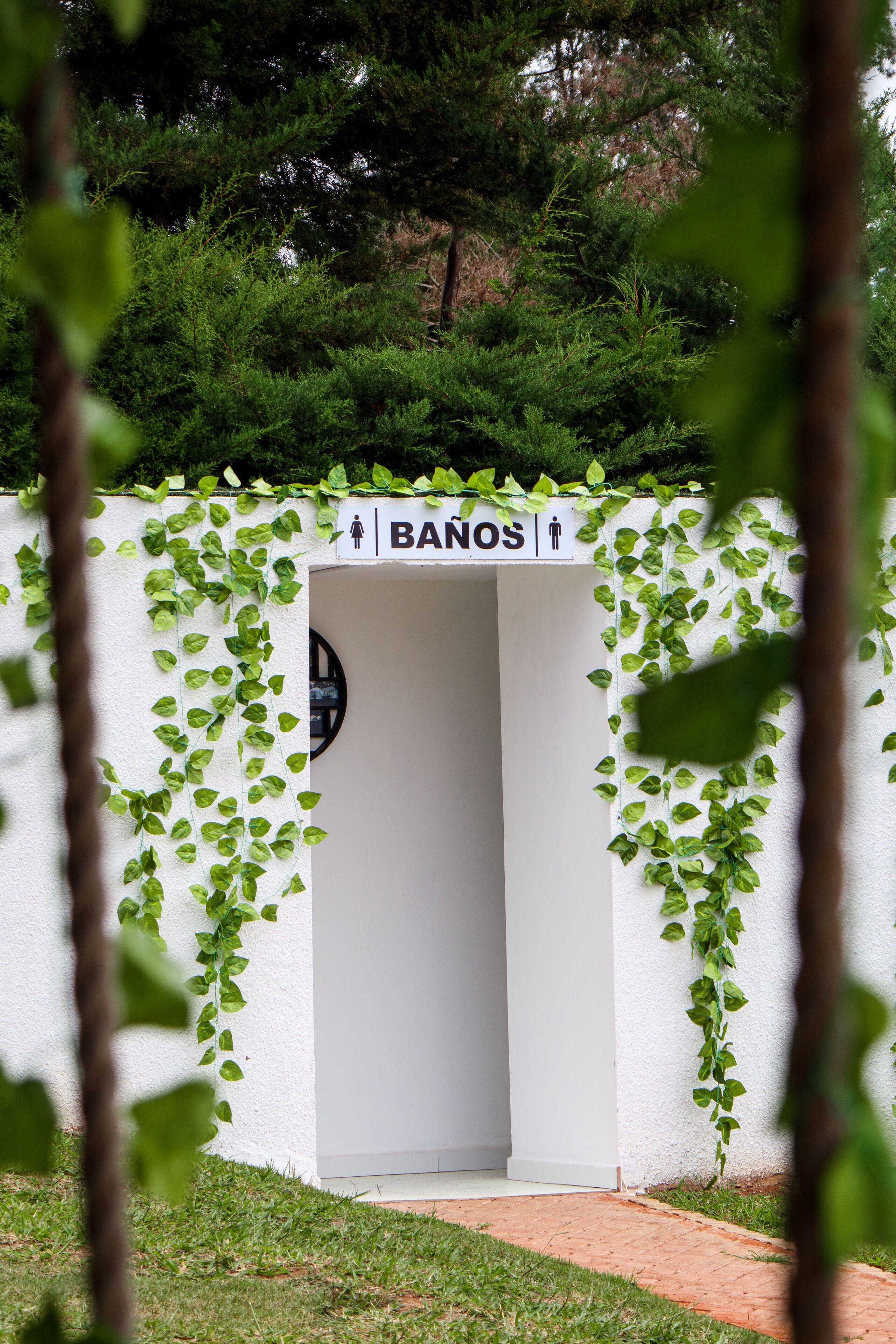 A white wall with a sign indicating a men's restroom, surrounded by greenery.