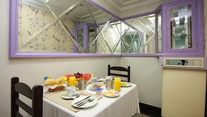 Un comedor con una mesa dispuesta para el desayuno, un espejo que refleja la habitación y ventanas con marcos morados.