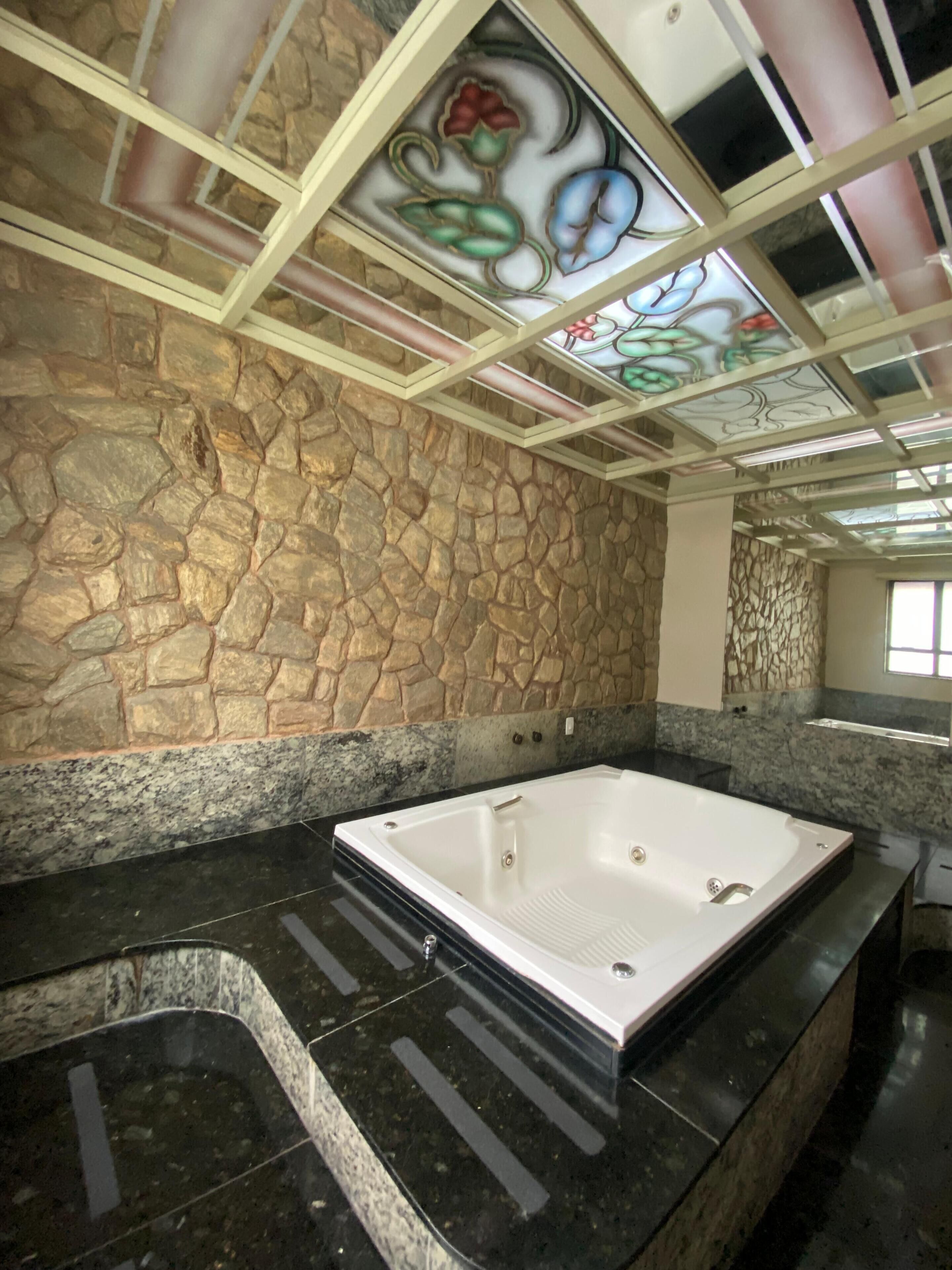 Un baño con pared de piedra, una bañera grande y techo con vidrieras de colores.