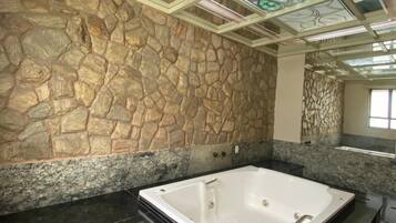 Un baño con pared de piedra, una bañera grande y techo con vidrieras de colores.