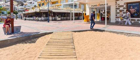 A beachside promenade with a wooden boardwalk leading to a restaurant named 'TAPAS'.