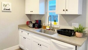 Una cocina con armarios blancos, una encimera, un lavabo, una ventana y una planta en maceta.