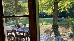 A patio with a table and chairs, a wooden deck, and a view of a grassy area with trees. - Spacious 3 BDR 3 BA 2 Acre property one minute from Lake Michigan-Dog Friendly! (Coloma)