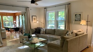 A living room with a beige sectional sofa, a glass coffee table, and a dining area with a wooden table and chairs. - Spacious 3 BDR 3 BA 2 Acre property one minute from Lake Michigan-Dog Friendly! (Coloma)