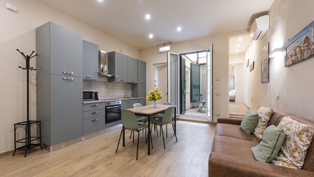 A modern kitchen with grey cabinets, a dining table with chairs, and a brown sofa with patterned cushions. - Mercato Contemporary Apartment by Mmega (Florence)