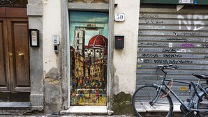 A door with a colorful mural, a bicycle, and a garage door with graffiti. - Mercato Contemporary Apartment by Mmega (Florence)